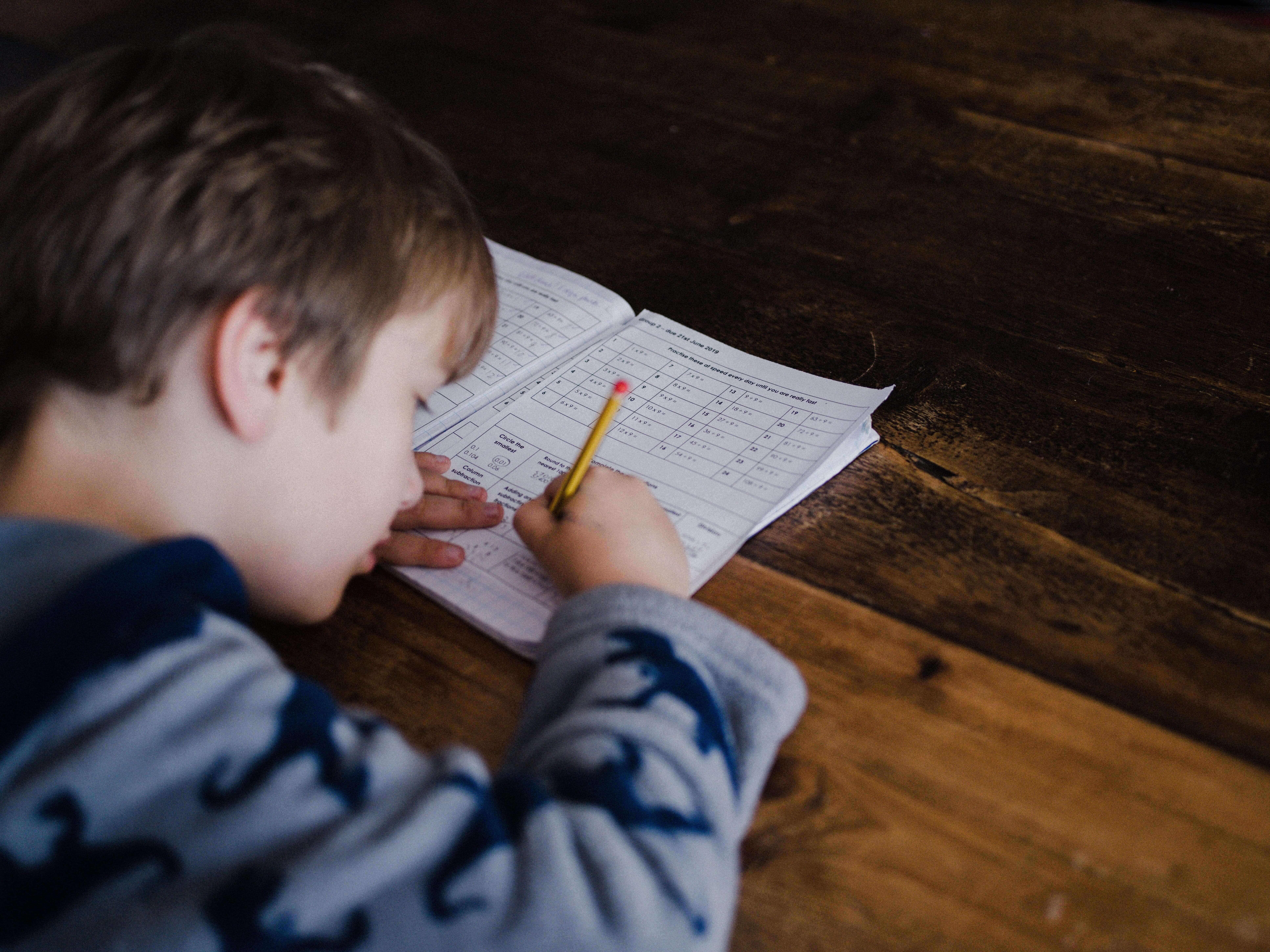 Neurodivergent student writing at a table while working on a school assignment at home